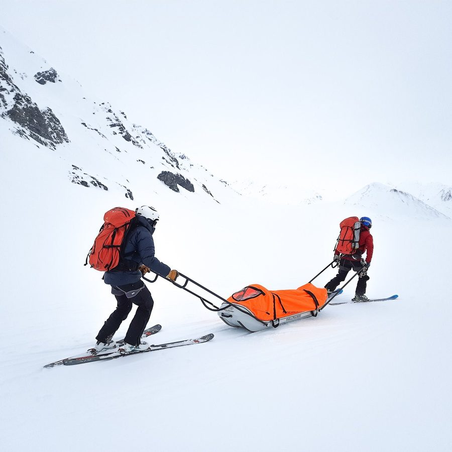 Two rescuers on skis with a sled in the winter mountains